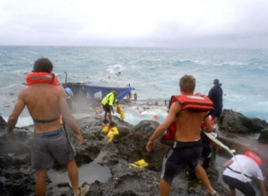 People clamber on the rocky shore on Christmas Island during a rescue attempt as a boat breaks up in the background this morning.