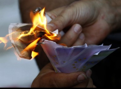 A protestor uses a burning €10 note to set fire to fake banknotes during an anti-austerity protest outside Greece's central bank in Athens today.