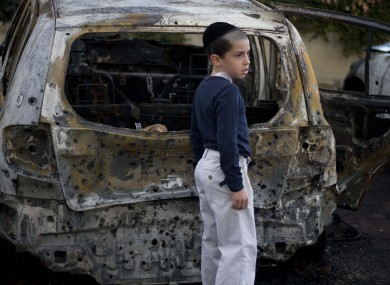 A boy stands next to a burned cars following Saturday night's rocket attacks from the Gaza Strip, in Ashdod, southern Israel