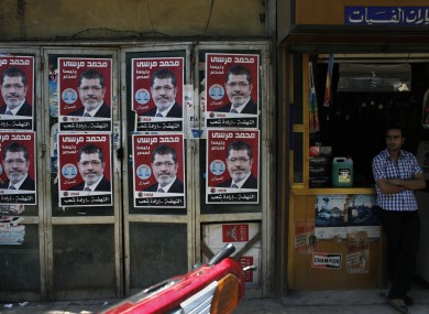 A worker stands in front of his shop next to posters with pictures of presidential candidate Mohammed Morsi