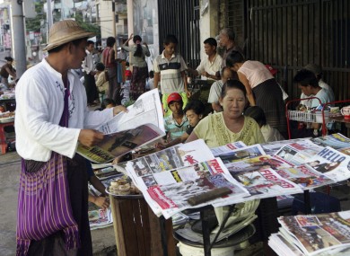 A man buys a weekly news journal at a roadside newspaper stand in Burma.